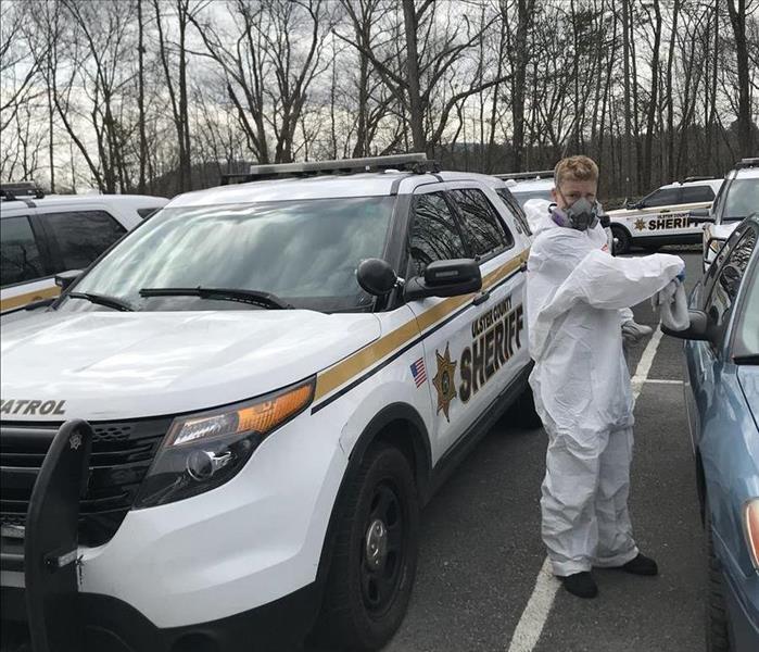 A police officer vehicle parked in a parking lot, with a man in a hazmat suit. 