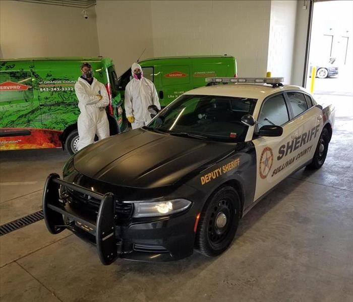 squad car inside warehouse with two tyvek donned employees